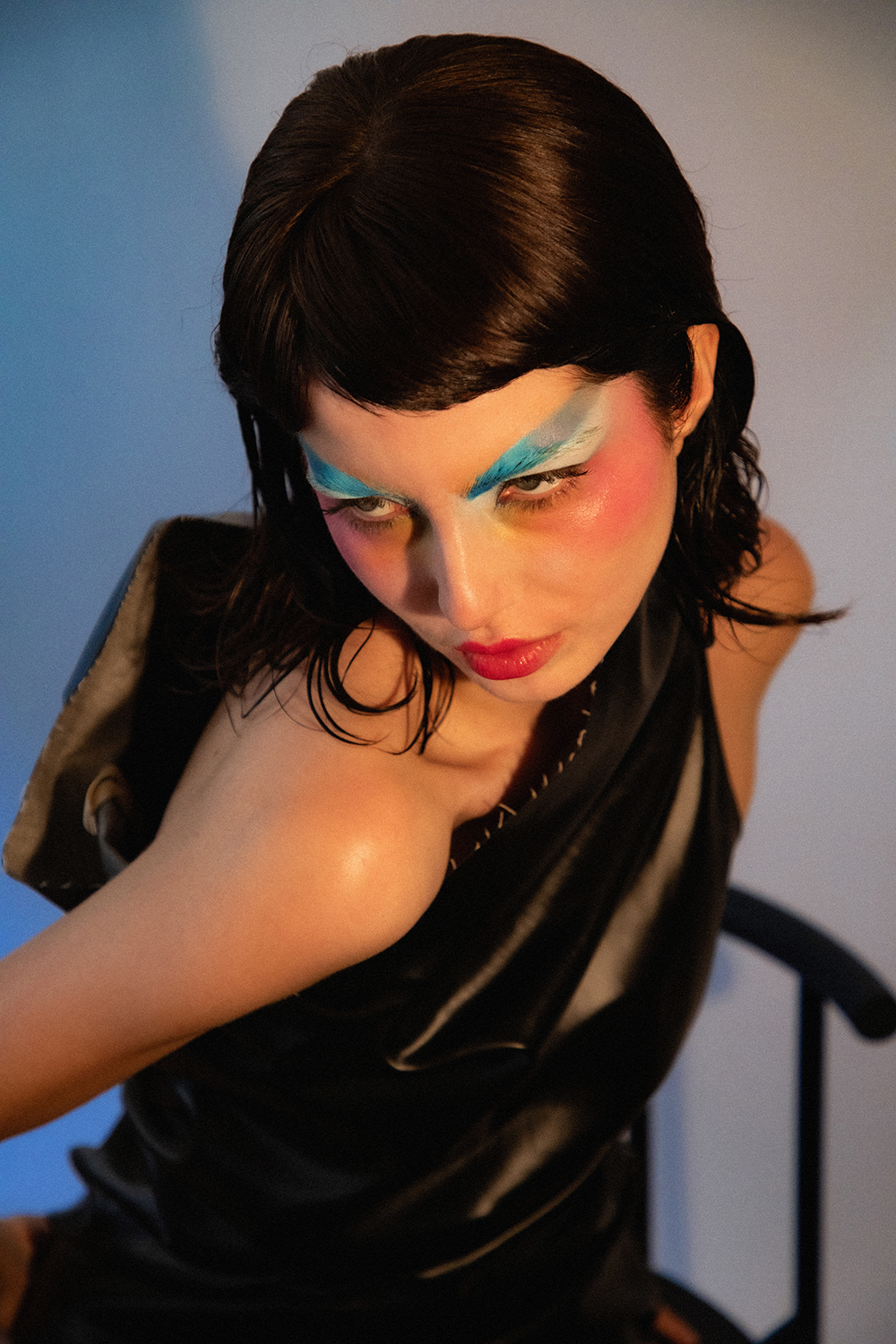 Close-up portrait of Autry with slicked dark hair and colorful makeup looking downwards over their shoulder